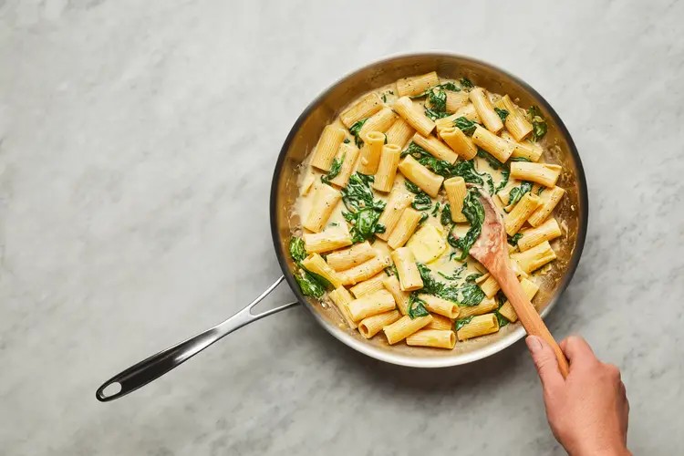 Tossing pasta and spinach in sauce
